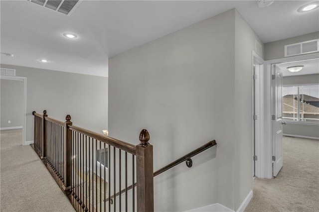 hallway featuring baseboards, light carpet, visible vents, and an upstairs landing