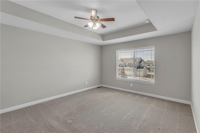 unfurnished room featuring ceiling fan, carpet floors, a tray ceiling, and baseboards