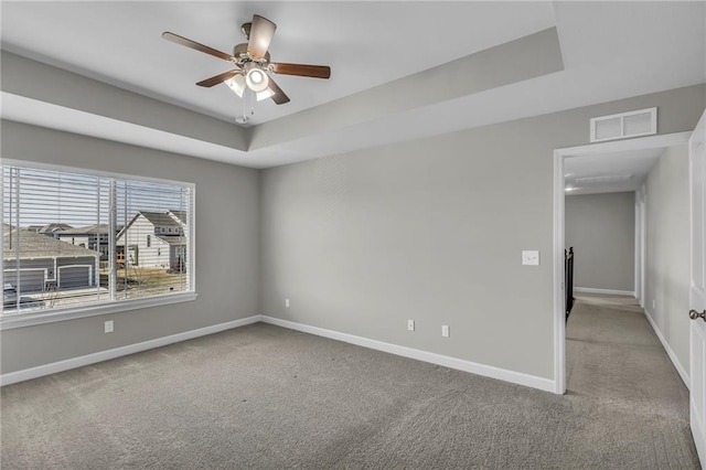 carpeted spare room with ceiling fan, a raised ceiling, visible vents, and baseboards