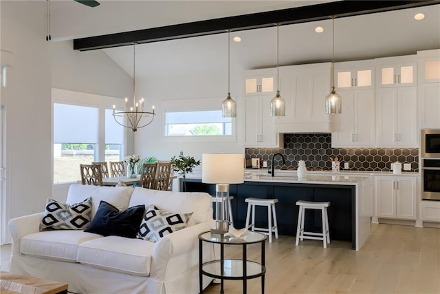 living area featuring vaulted ceiling with beams, light wood finished floors, and an inviting chandelier