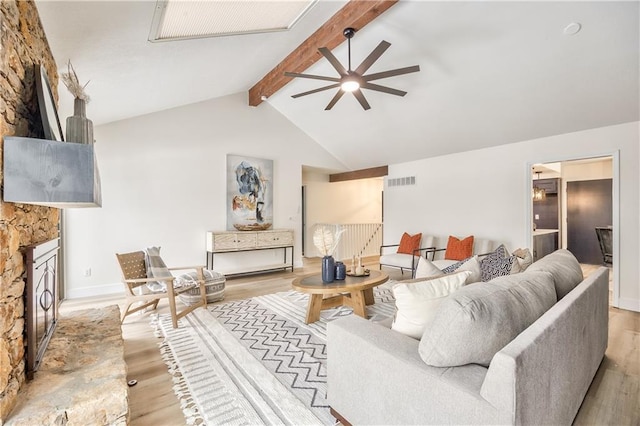 living room with ceiling fan, a fireplace, light hardwood / wood-style floors, and vaulted ceiling with beams