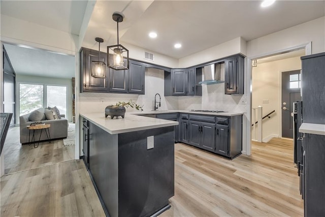 kitchen with pendant lighting, stainless steel gas stovetop, kitchen peninsula, wall chimney range hood, and light wood-type flooring