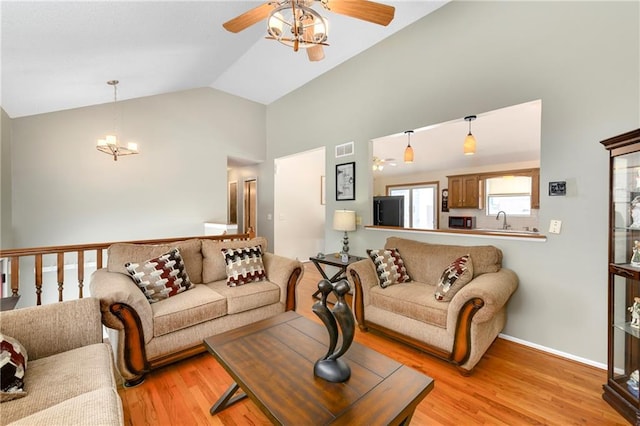 living room featuring vaulted ceiling, ceiling fan with notable chandelier, visible vents, and light wood-type flooring