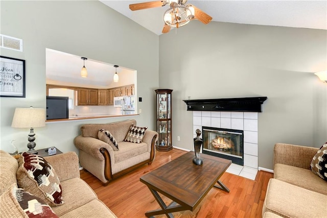 living area with visible vents, high vaulted ceiling, a fireplace, ceiling fan, and light wood-type flooring