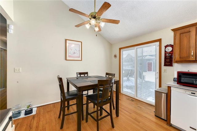 dining room with visible vents, ceiling fan, vaulted ceiling, light wood-style floors, and a textured ceiling