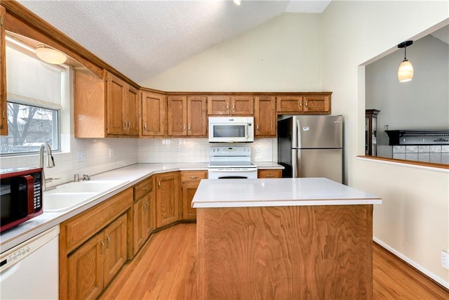 kitchen featuring white appliances, brown cabinets, vaulted ceiling, light wood-type flooring, and a center island