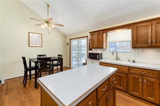 kitchen with brown cabinets, a sink, backsplash, black microwave, and vaulted ceiling