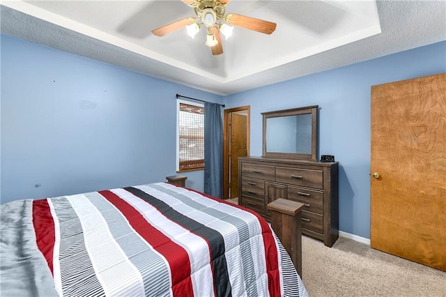 bedroom with baseboards, ceiling fan, a textured ceiling, a raised ceiling, and light carpet