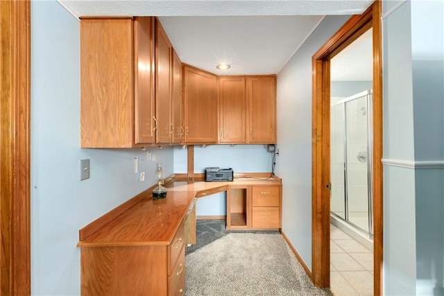 office space with light tile patterned floors, built in desk, light colored carpet, and baseboards