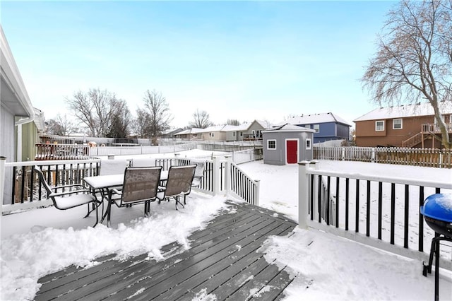 snow covered deck featuring outdoor dining space, a fenced backyard, an outdoor structure, a storage shed, and a residential view