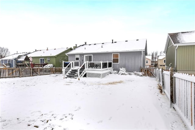 snow covered house featuring a residential view, a wooden deck, and a fenced backyard