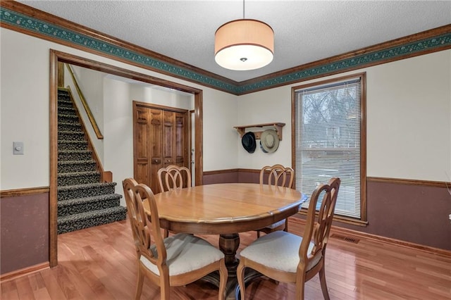 dining area featuring ornamental molding, a textured ceiling, and light wood-type flooring