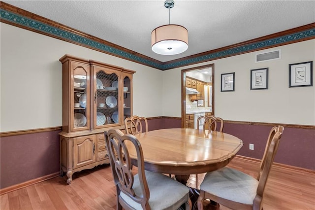 dining area featuring crown molding, light hardwood / wood-style floors, and a textured ceiling