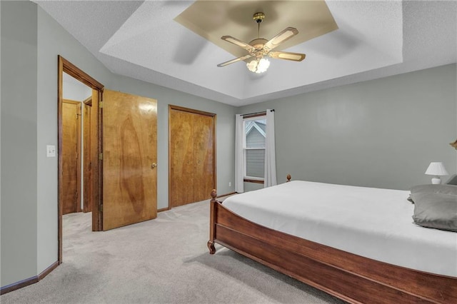 bedroom featuring ceiling fan, a raised ceiling, light carpet, and a textured ceiling