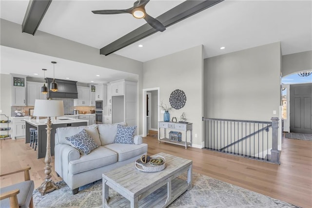 living room featuring ceiling fan, light wood-type flooring, and beam ceiling