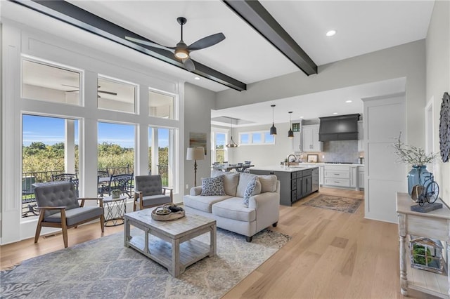 living room with sink, light hardwood / wood-style flooring, beamed ceiling, and ceiling fan