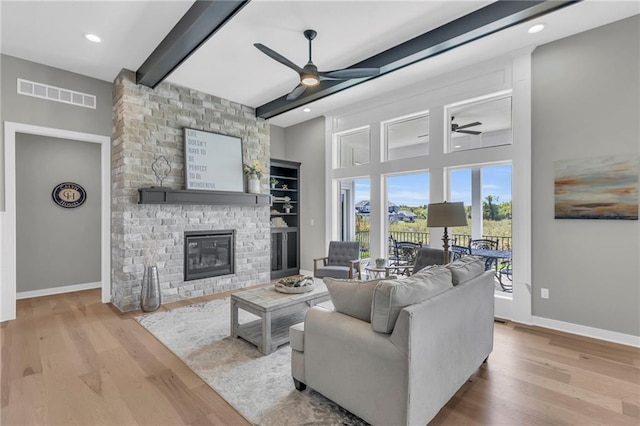 living room with ceiling fan, beam ceiling, a brick fireplace, and light hardwood / wood-style flooring