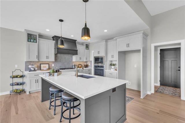 kitchen with pendant lighting, sink, a kitchen island with sink, built in microwave, and oven