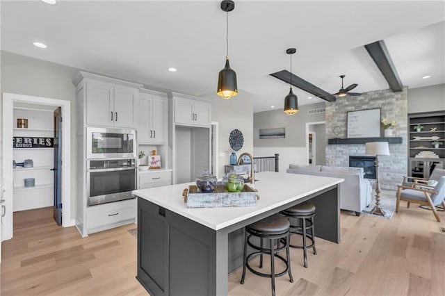 kitchen with appliances with stainless steel finishes, a kitchen island with sink, hanging light fixtures, white cabinetry, and a fireplace