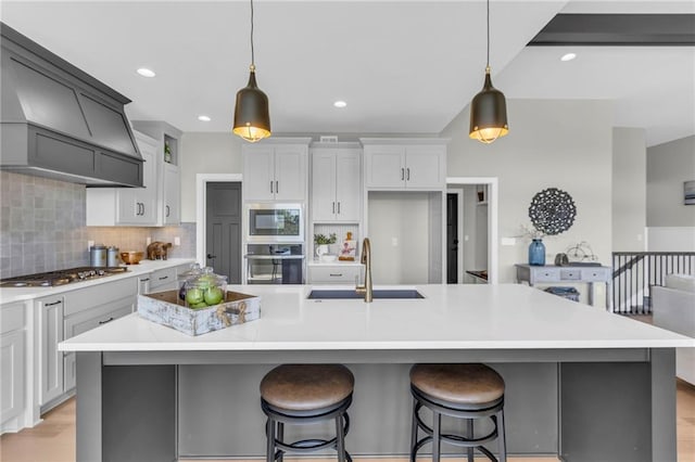 kitchen with hanging light fixtures, custom exhaust hood, appliances with stainless steel finishes, and a large island with sink