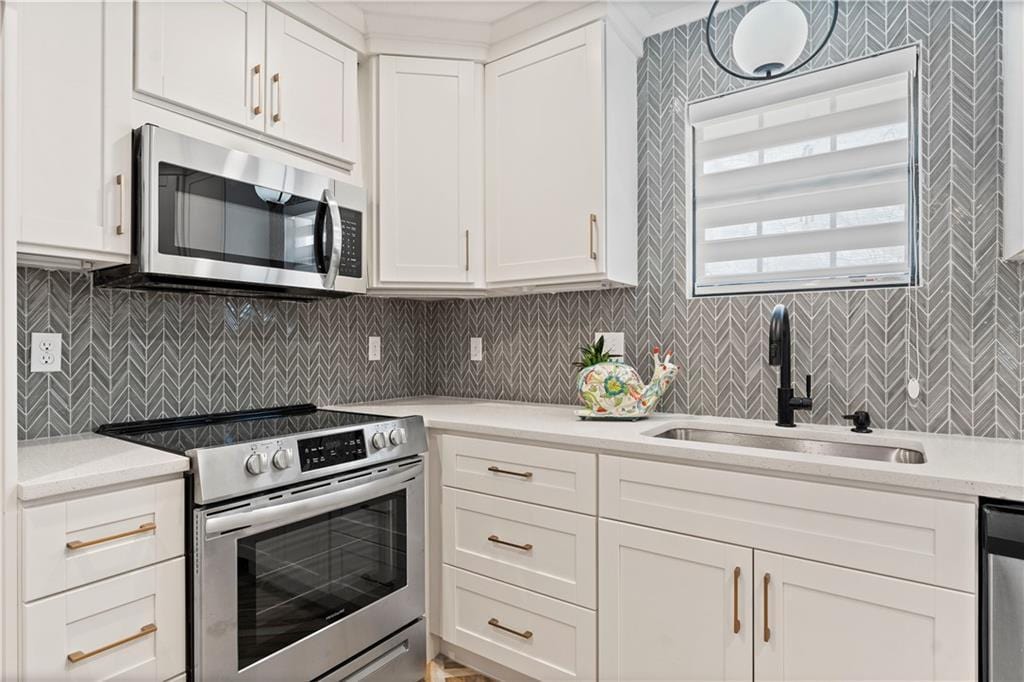 kitchen featuring stainless steel appliances, light countertops, a sink, and white cabinetry