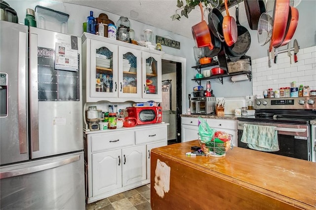 kitchen with appliances with stainless steel finishes, white cabinets, glass insert cabinets, and decorative backsplash