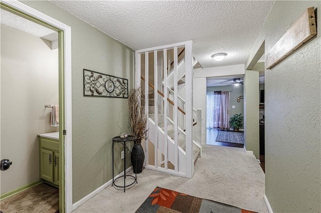 corridor featuring stairs, baseboards, a textured ceiling, and a textured wall