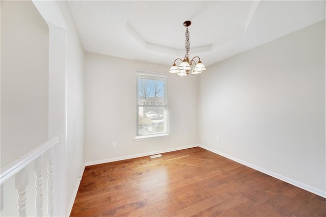 empty room featuring a tray ceiling, wood finished floors, baseboards, and a chandelier