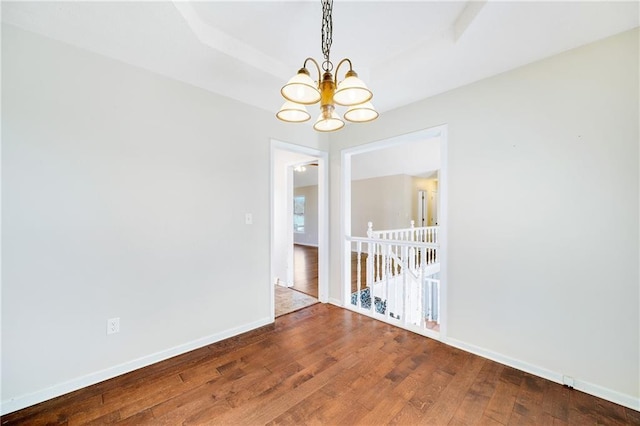 spare room featuring a notable chandelier, baseboards, and wood-type flooring