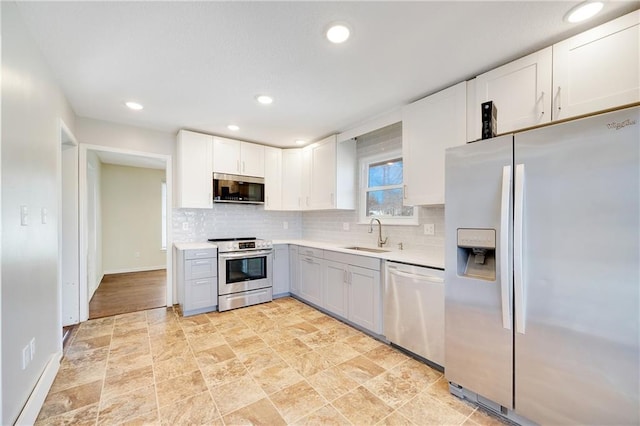 kitchen featuring light countertops, decorative backsplash, appliances with stainless steel finishes, white cabinets, and a sink