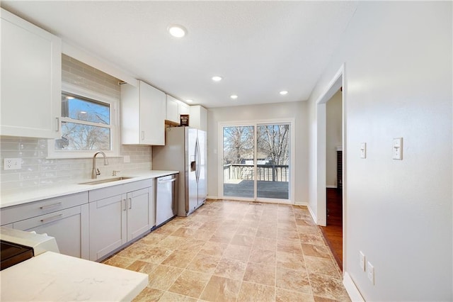 kitchen featuring baseboards, dishwasher, light countertops, decorative backsplash, and a sink