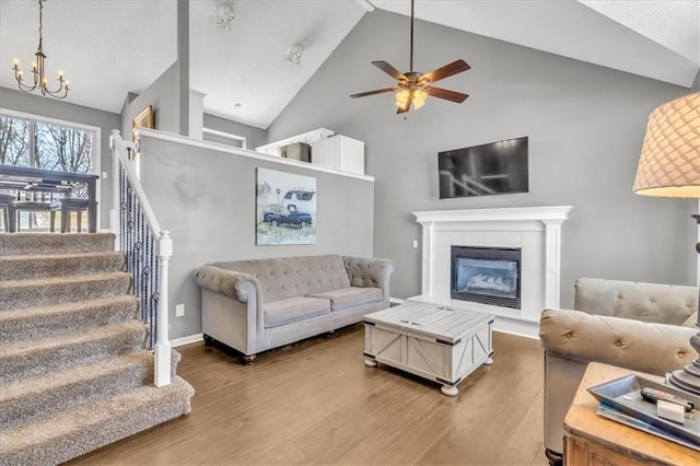 living area featuring baseboards, a tiled fireplace, wood finished floors, stairs, and ceiling fan with notable chandelier