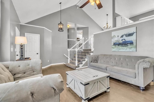 living area with high vaulted ceiling, ceiling fan with notable chandelier, wood finished floors, baseboards, and stairway