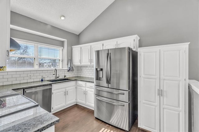 kitchen with lofted ceiling, stainless steel appliances, a sink, white cabinets, and dark countertops