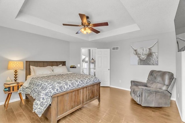 bedroom with baseboards, visible vents, ceiling fan, wood finished floors, and a tray ceiling