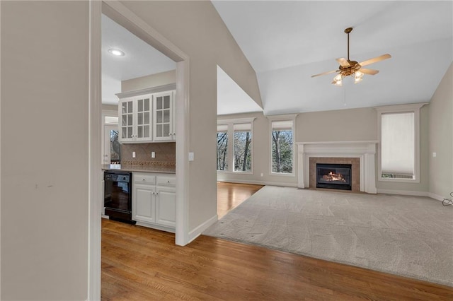 unfurnished living room featuring light wood-type flooring, lofted ceiling, a ceiling fan, wet bar, and baseboards