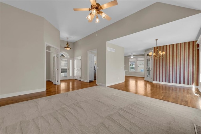 unfurnished living room with ceiling fan with notable chandelier, high vaulted ceiling, baseboards, and wood finished floors