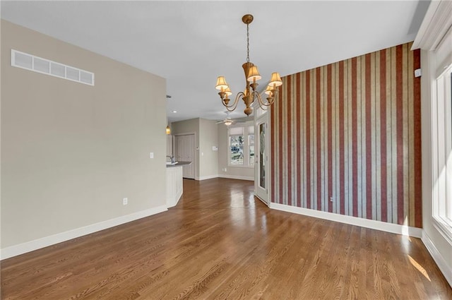 unfurnished dining area featuring baseboards, wood finished floors, visible vents, and a chandelier