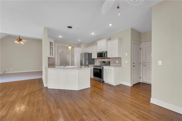 kitchen with a ceiling fan, light wood-style floors, appliances with stainless steel finishes, a peninsula, and decorative backsplash