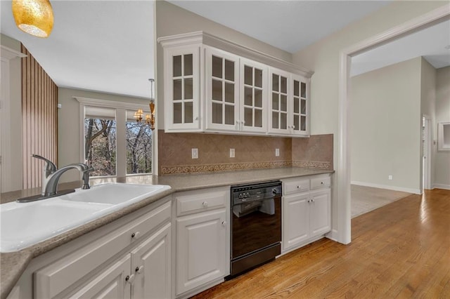 kitchen featuring a notable chandelier, light wood-style flooring, a sink, black dishwasher, and decorative backsplash