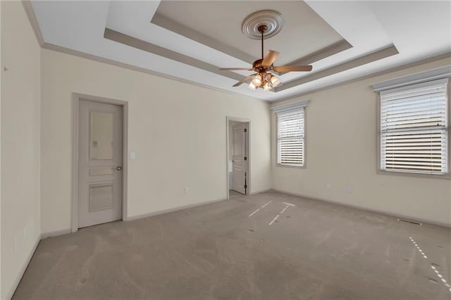 empty room featuring light carpet, ceiling fan, baseboards, and a tray ceiling