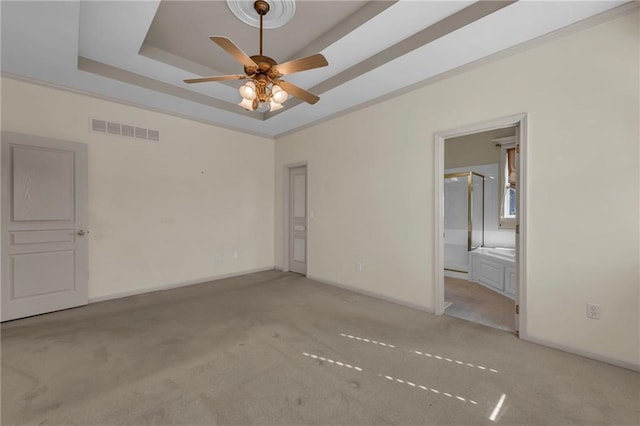 carpeted empty room with visible vents, baseboards, a raised ceiling, and ceiling fan