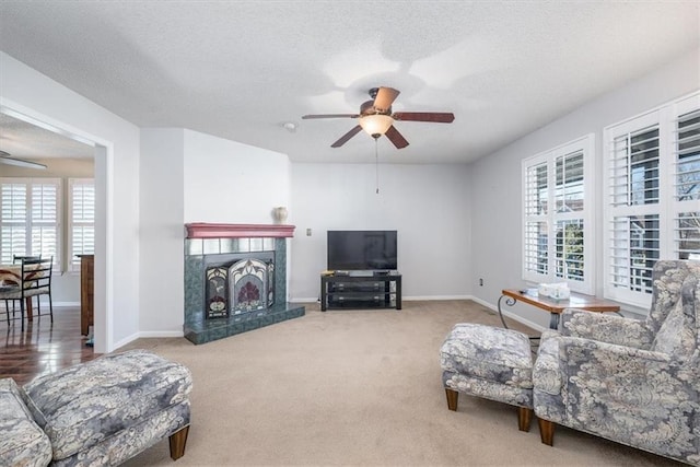 living room with a tile fireplace, carpet, a textured ceiling, and ceiling fan