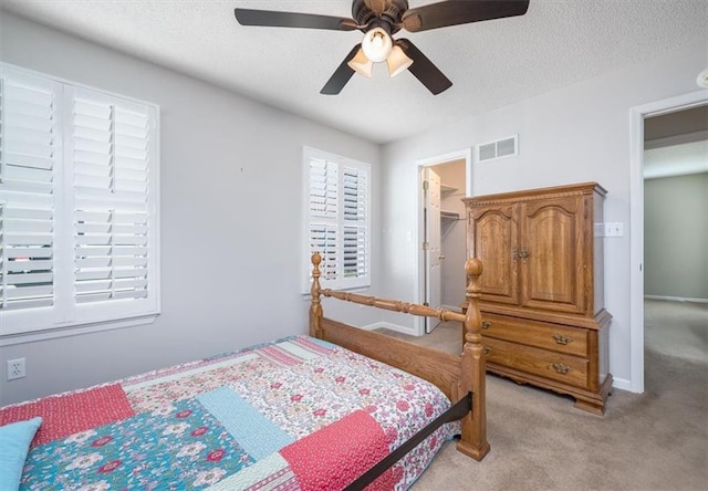 bedroom featuring ceiling fan, a walk in closet, light colored carpet, and a textured ceiling