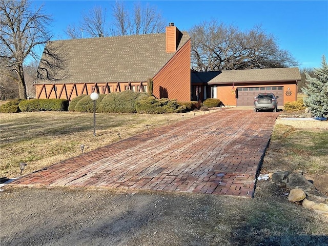 view of property exterior featuring decorative driveway, a garage, a yard, and a chimney