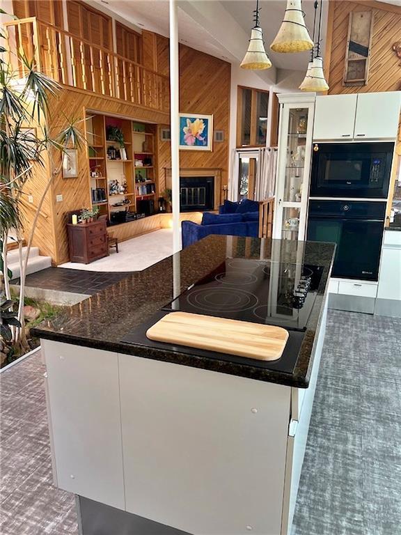 kitchen with white cabinetry, black appliances, dark countertops, and wood walls