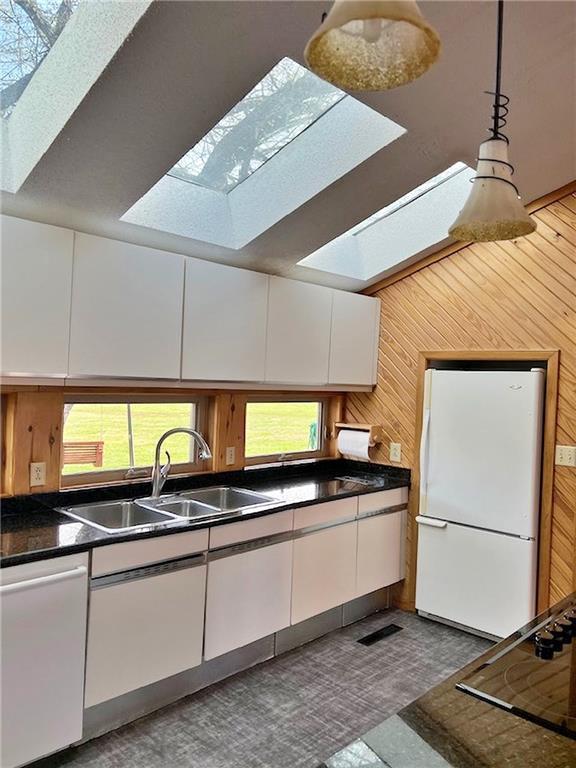 kitchen with freestanding refrigerator, dishwashing machine, a sink, and white cabinets
