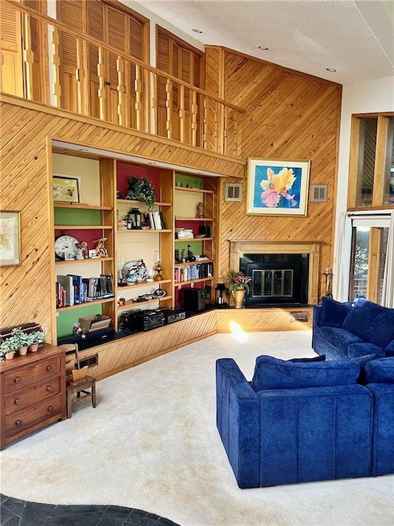 living area featuring visible vents, high vaulted ceiling, wood walls, and a glass covered fireplace