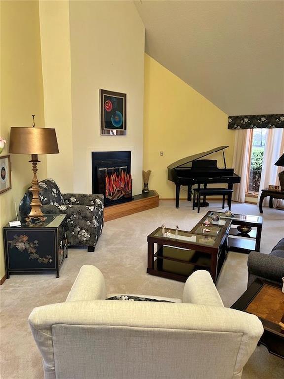 living room featuring carpet flooring, baseboards, lofted ceiling, and a glass covered fireplace