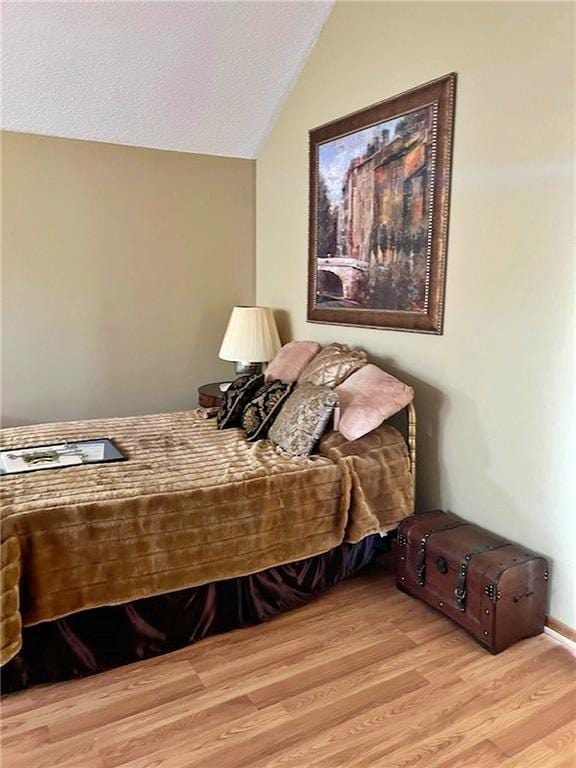 bedroom with a textured ceiling, wood finished floors, and vaulted ceiling